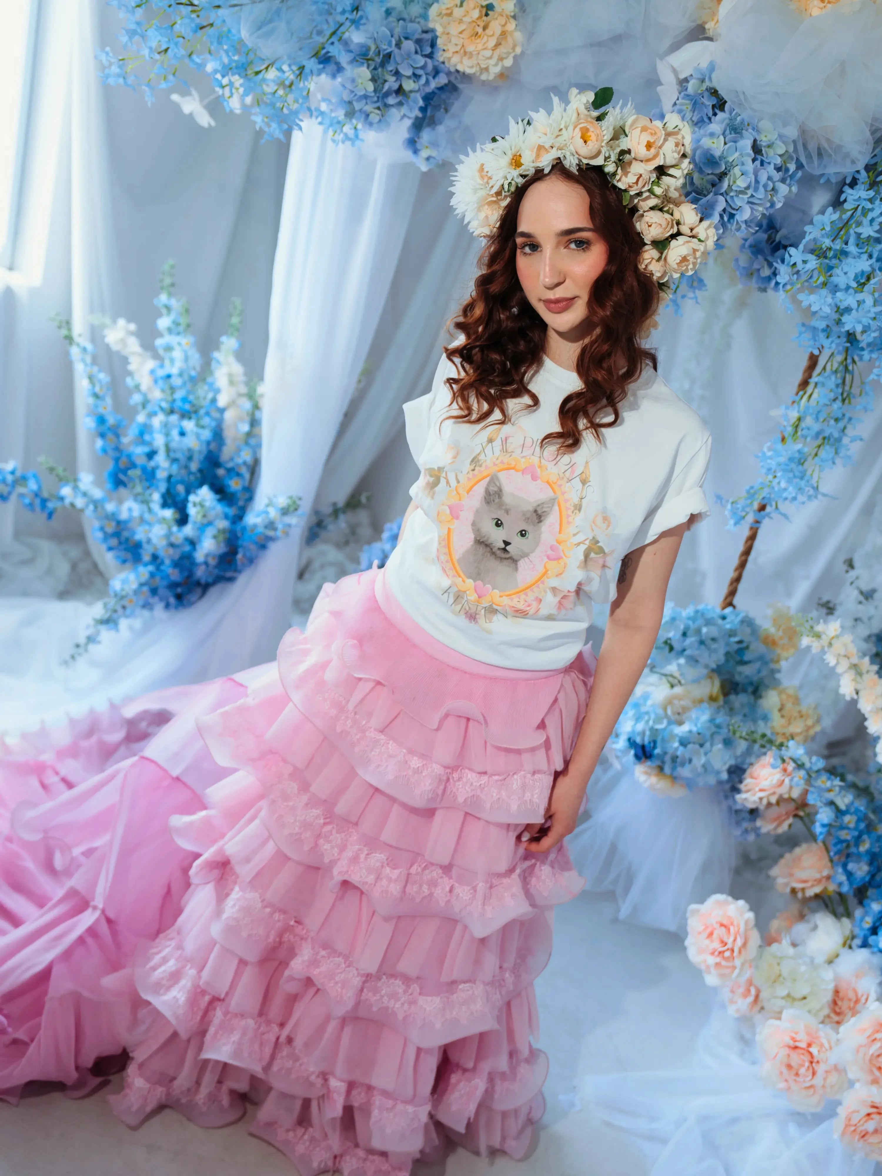 A woman wearing the dahlia pink ruffle skirt styled with a floral crown and kitten tee, highlighting the dramatic pink train and layered ruffles.