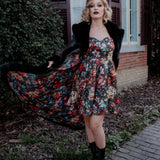 A woman wearing a stained glass satin mini dress and a black coat, standing outdoors near a building.