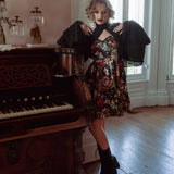 A woman wearing the Stained Rose Darling Dress, standing next to an old piano in a room with large windows.