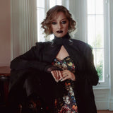 A woman wearing a stained glass satin mini dress and a dark coat in an elegant room.