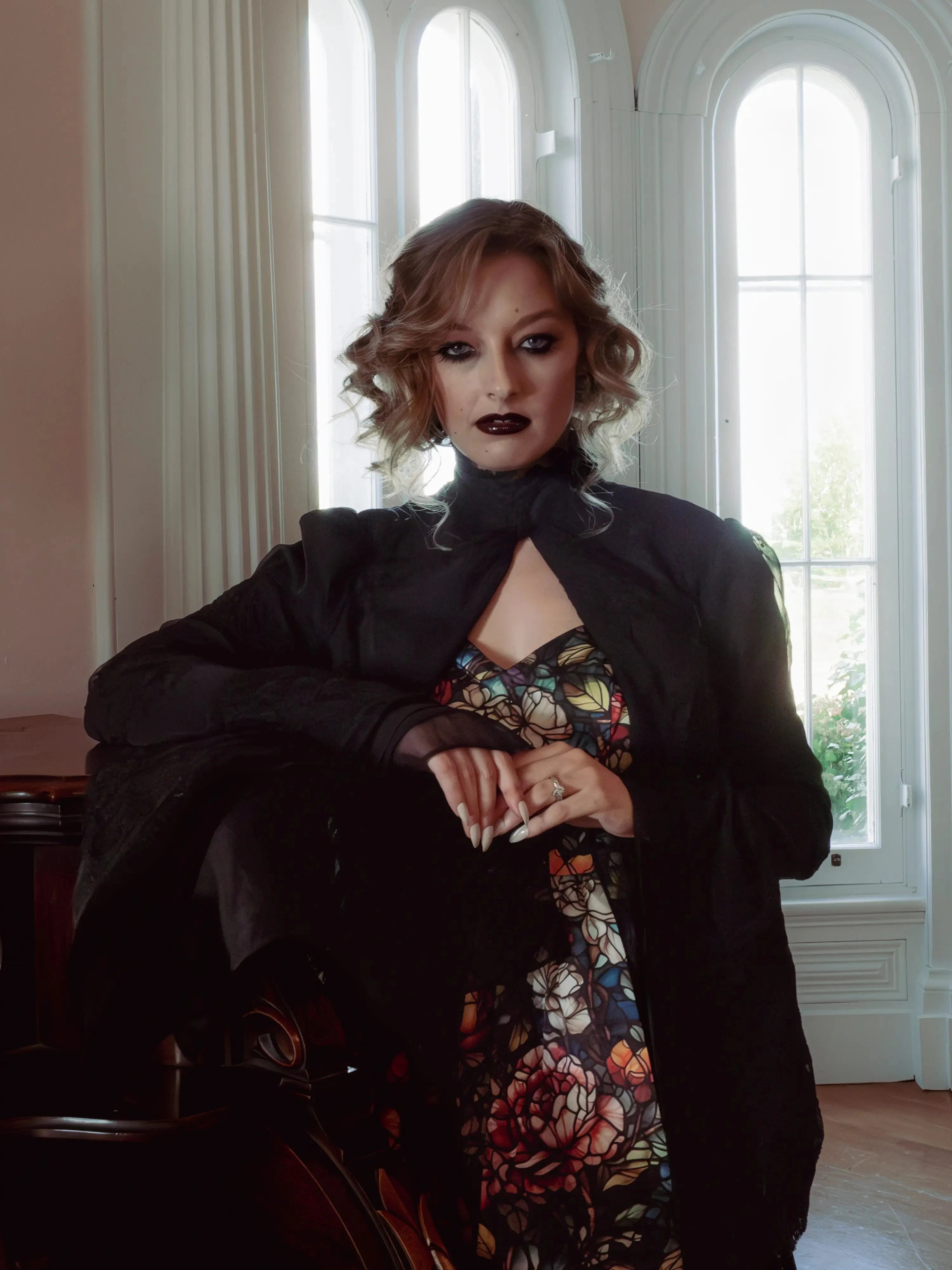A woman wearing a stained glass satin mini dress and a dark coat in an elegant room.