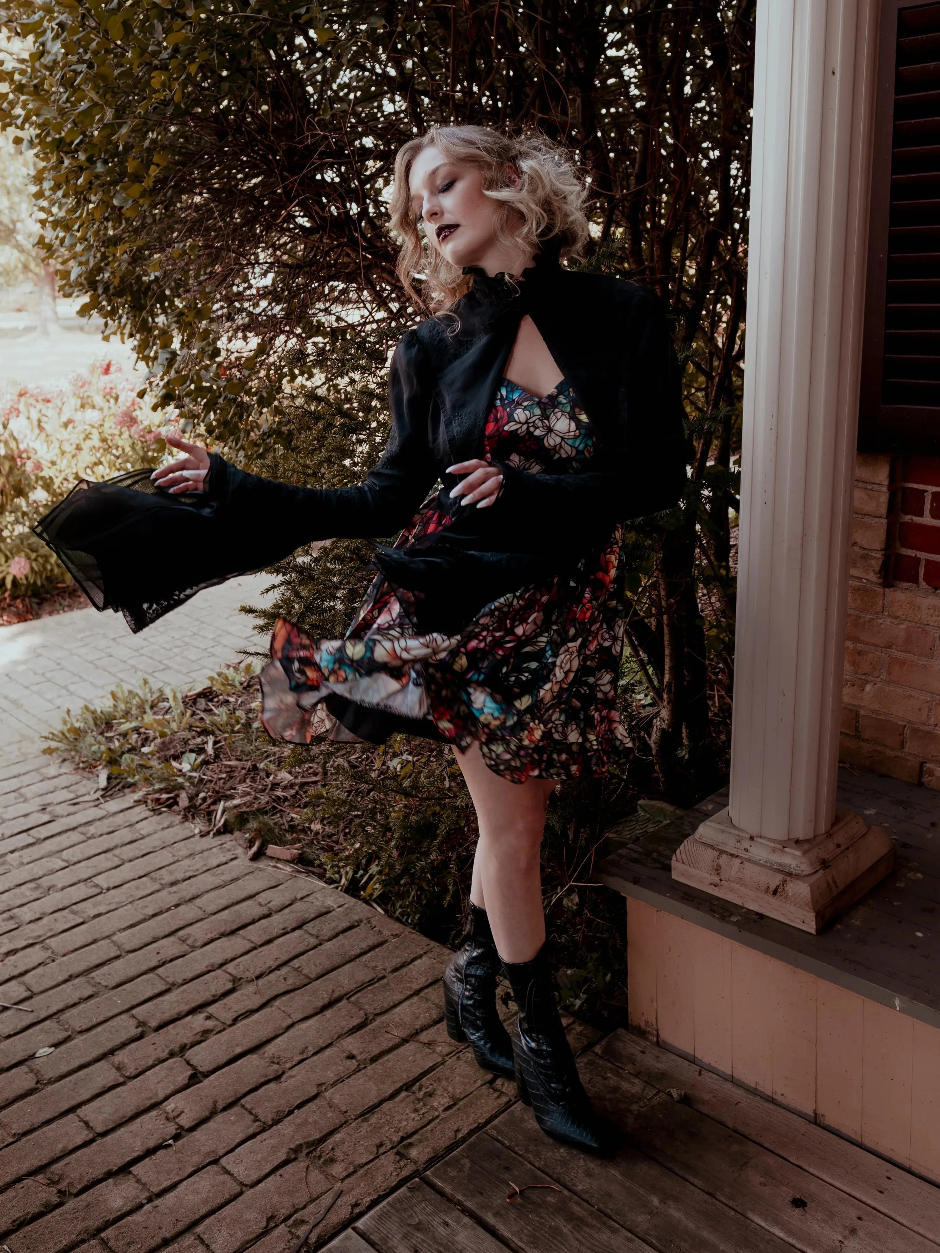 A woman wearing the Stained Rose Darling Dress and a black jacket, standing on a porch.