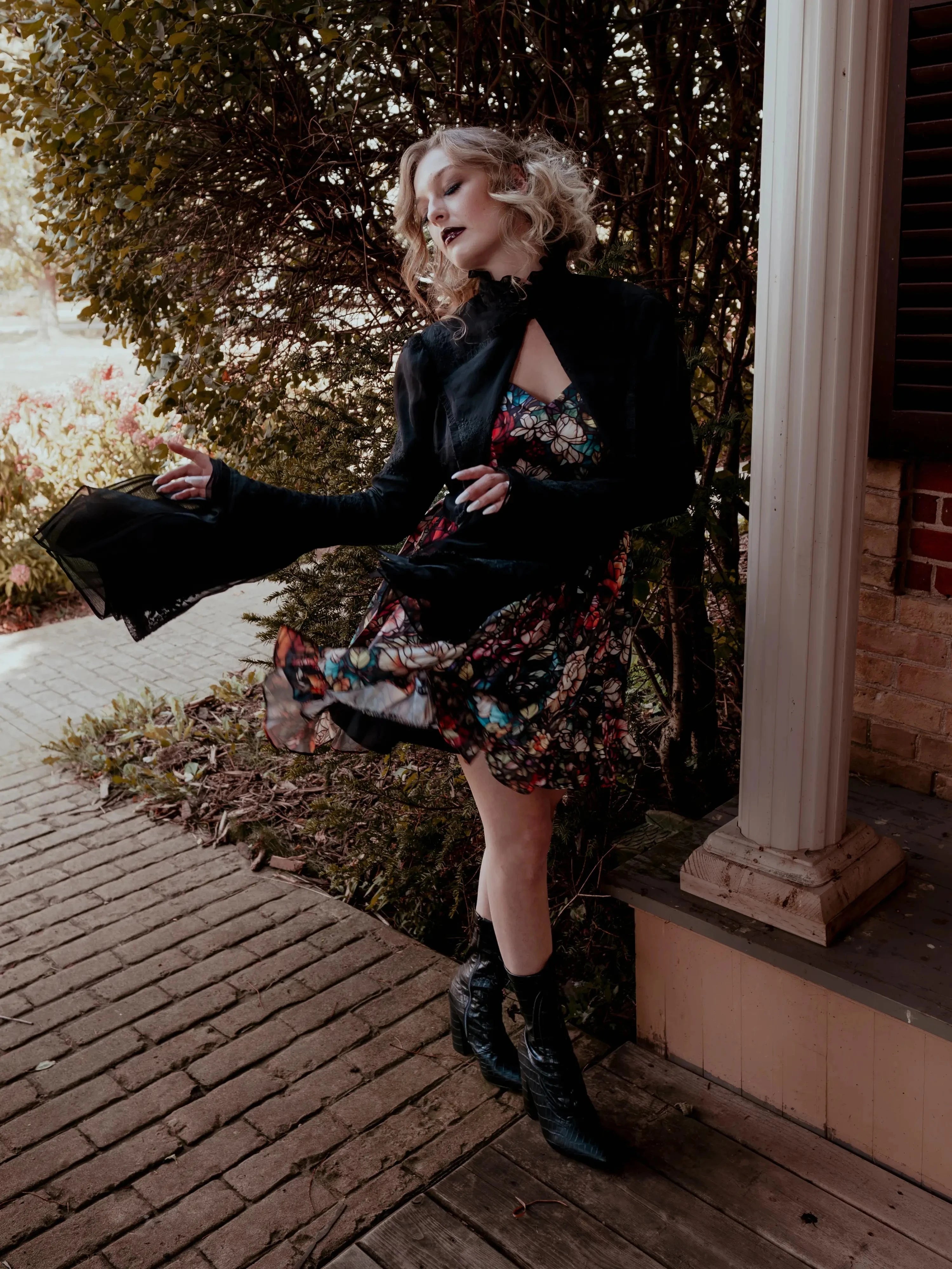 A woman wearing the Stained Rose Darling Dress and a black jacket, standing on a porch.