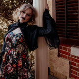 A woman wearing the Stained Rose Darling Dress, leaning against a brick wall with a window.