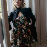 A woman wearing a stained glass satin mini dress and a dark jacket, standing in a doorway.