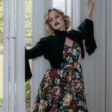 A woman wearing a stained glass satin mini dress and a black jacket stood before a white door.