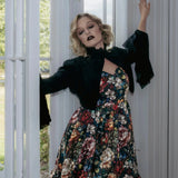 A woman wearing a stained glass satin mini dress and a black jacket stood before a white door.