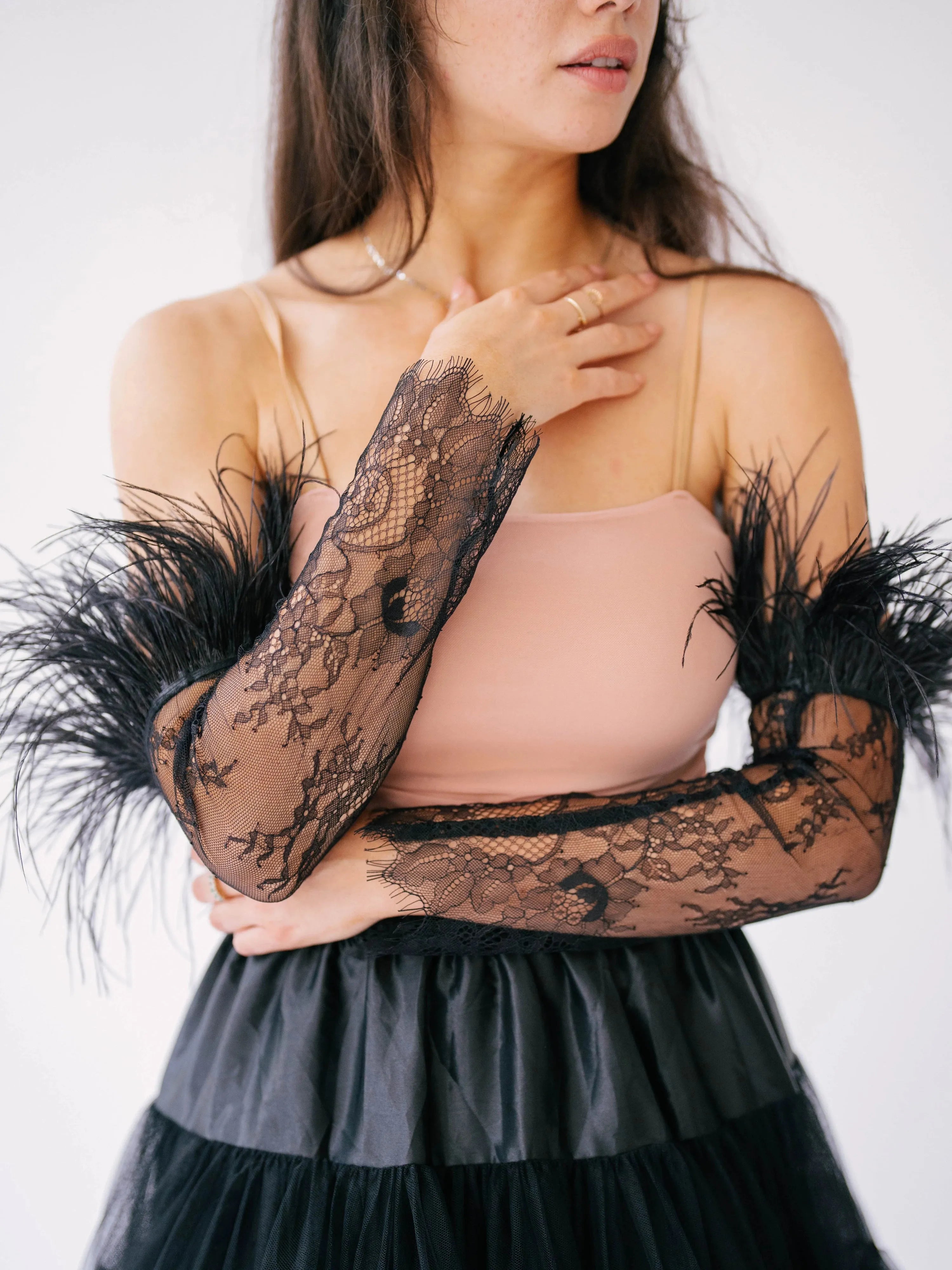 The Eleanor Black Feather Gloves paired with a black tulle skirt and nude top, emphasizing the gloves' gothic lace and feather embellishments.
