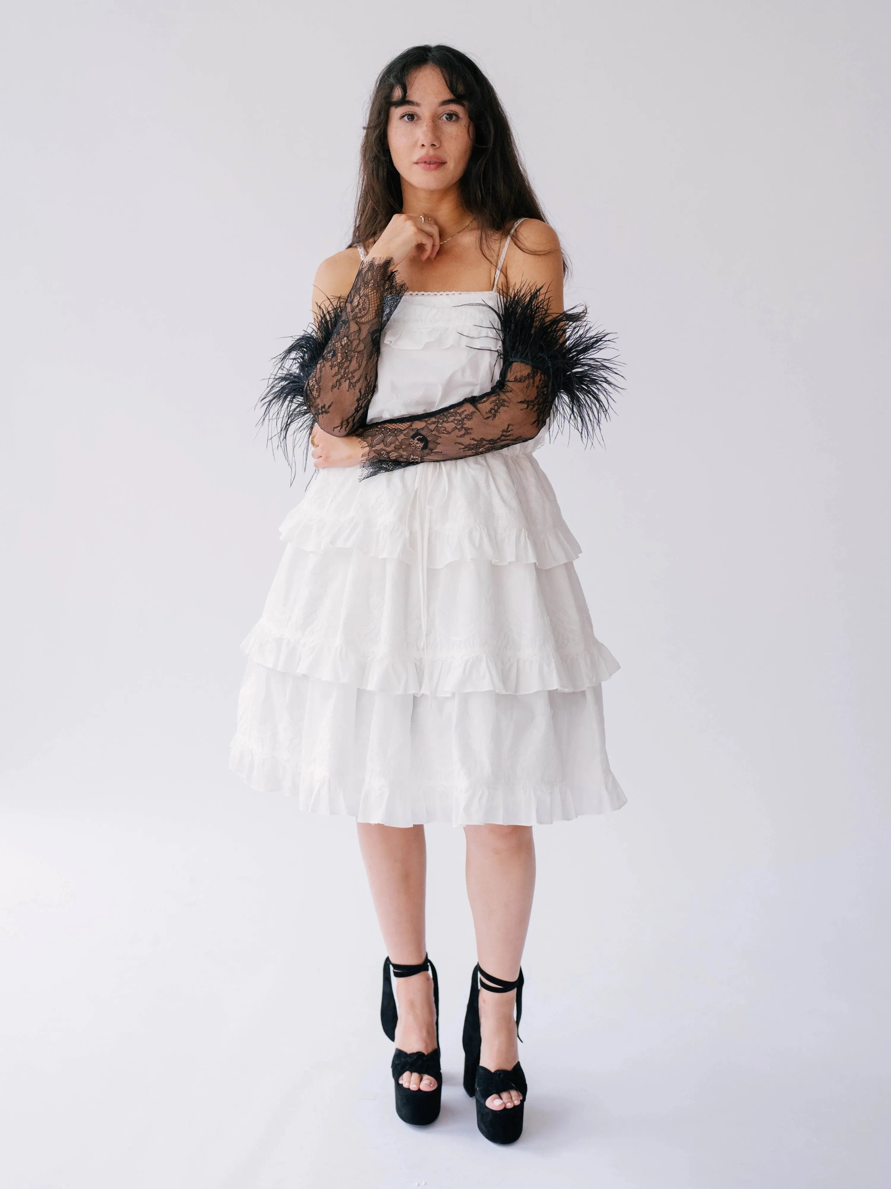 Full-body view of The Eleanor Black Feather Gloves styled with a white layered dress and black heels.