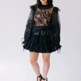The Eleanor Midnight Black Lace Top with sheer floral lace, ruffled collar, and voluminous sleeves styled with a black mini skirt.