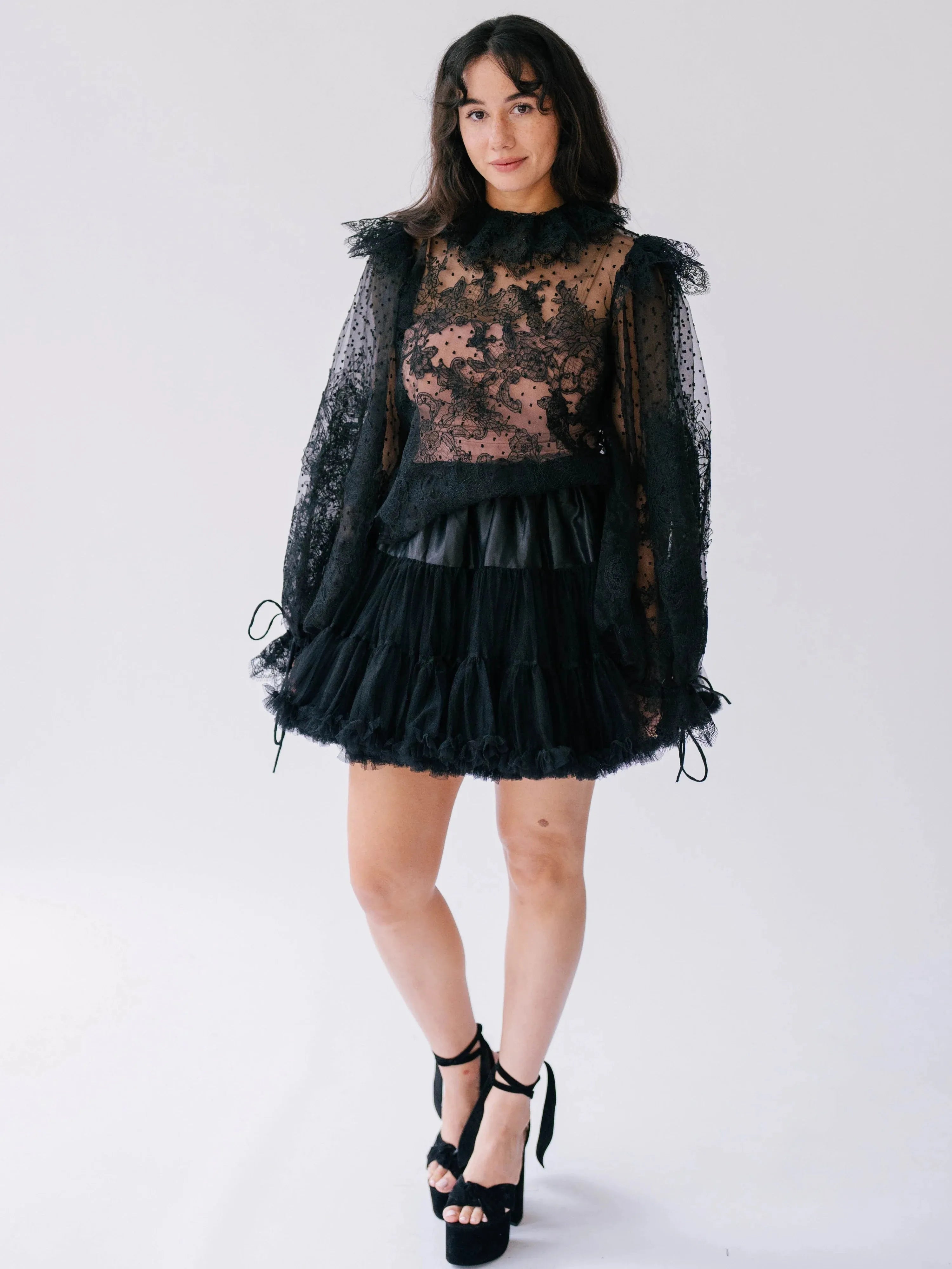 The Eleanor Midnight Black Lace Top with sheer floral lace, ruffled collar, and voluminous sleeves styled with a black mini skirt.