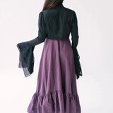 A back view of a woman wearing a purple midi dress with a black lace bolero jacket over top.