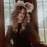 A woman in a black cotton dress with a decorative headpiece in a room with large windows.