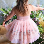 Back view of a woman in a pink tutu dress standing in front of floral decorations.