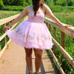 A woman in a pink tutu dress standing on a wooden bridge in a natural setting.