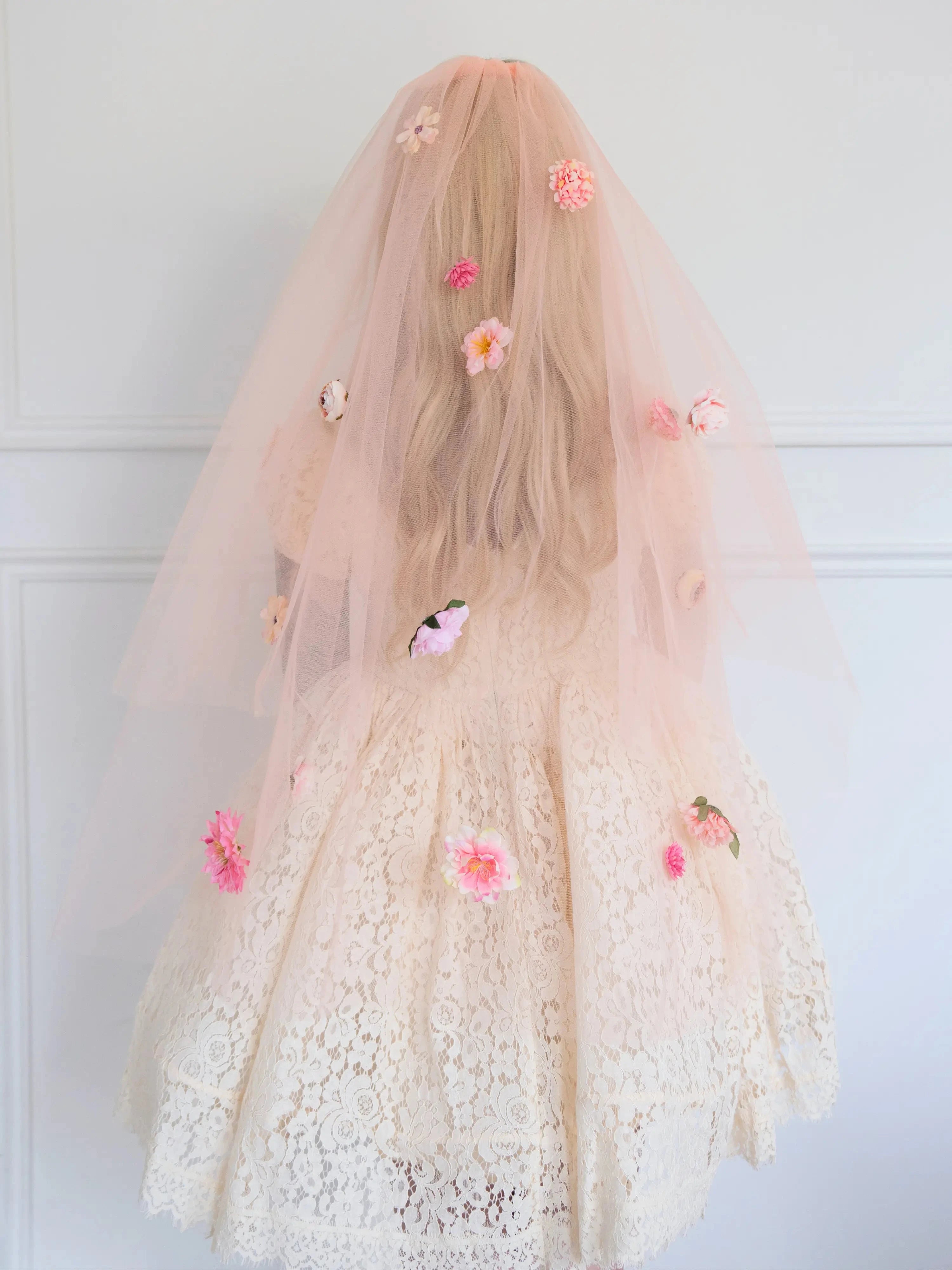 Back view of the Secret Garden Floral Veil featuring layered peach tulle and vibrant pink flowers. Worn by a woman in a white lace dress.