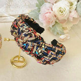 Colorful tweed headband with intricate patterns and knotted design on a table with florals in the background.