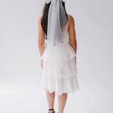 A woman wearing a white bridal mini dress with black lace-up platform shoes, and the Ivory Grand Bridal Hair Bow in her hair, viewed from the back.