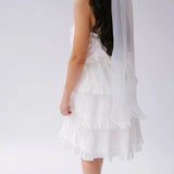 A woman wearing a white dress with a white bridal hair bow, showcasing the long tails on a plain background.