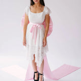 A woman wearing a white lace dress with a large pink bow belt and black platform heels for a statement look.