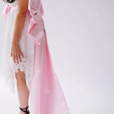 A woman wearing a white lace mini dress featuring the Ballet Pink Grand Bow Belt.