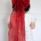A plus-sized woman wearing a large red hair bow and a lace maxi dress, against a white background.
