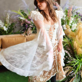 A woman in a flowing white lace corset top surrounded by florals.
