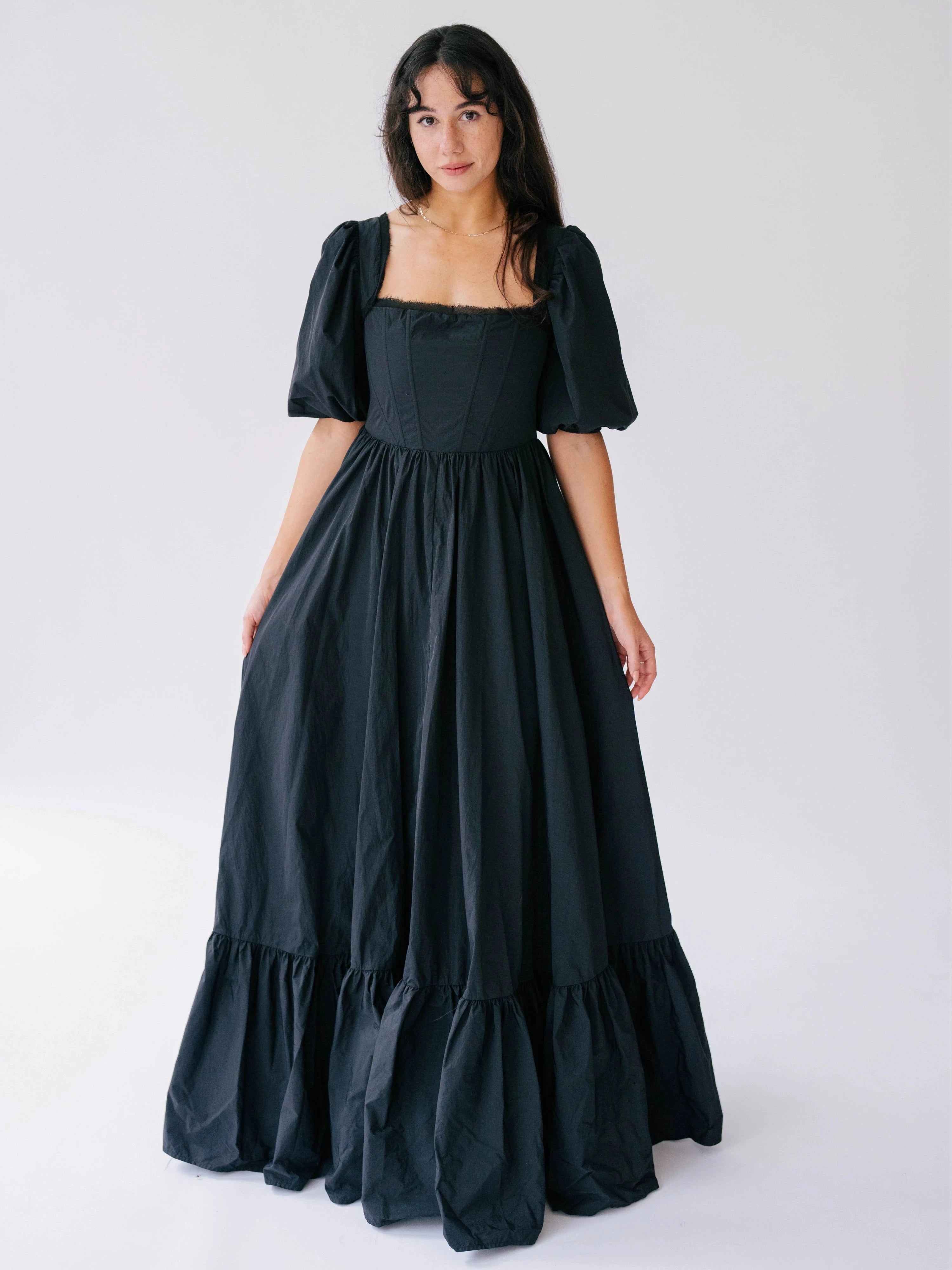 A woman wearing a black taffeta corset gown with puff sleeves and a tiered ruffle hem.