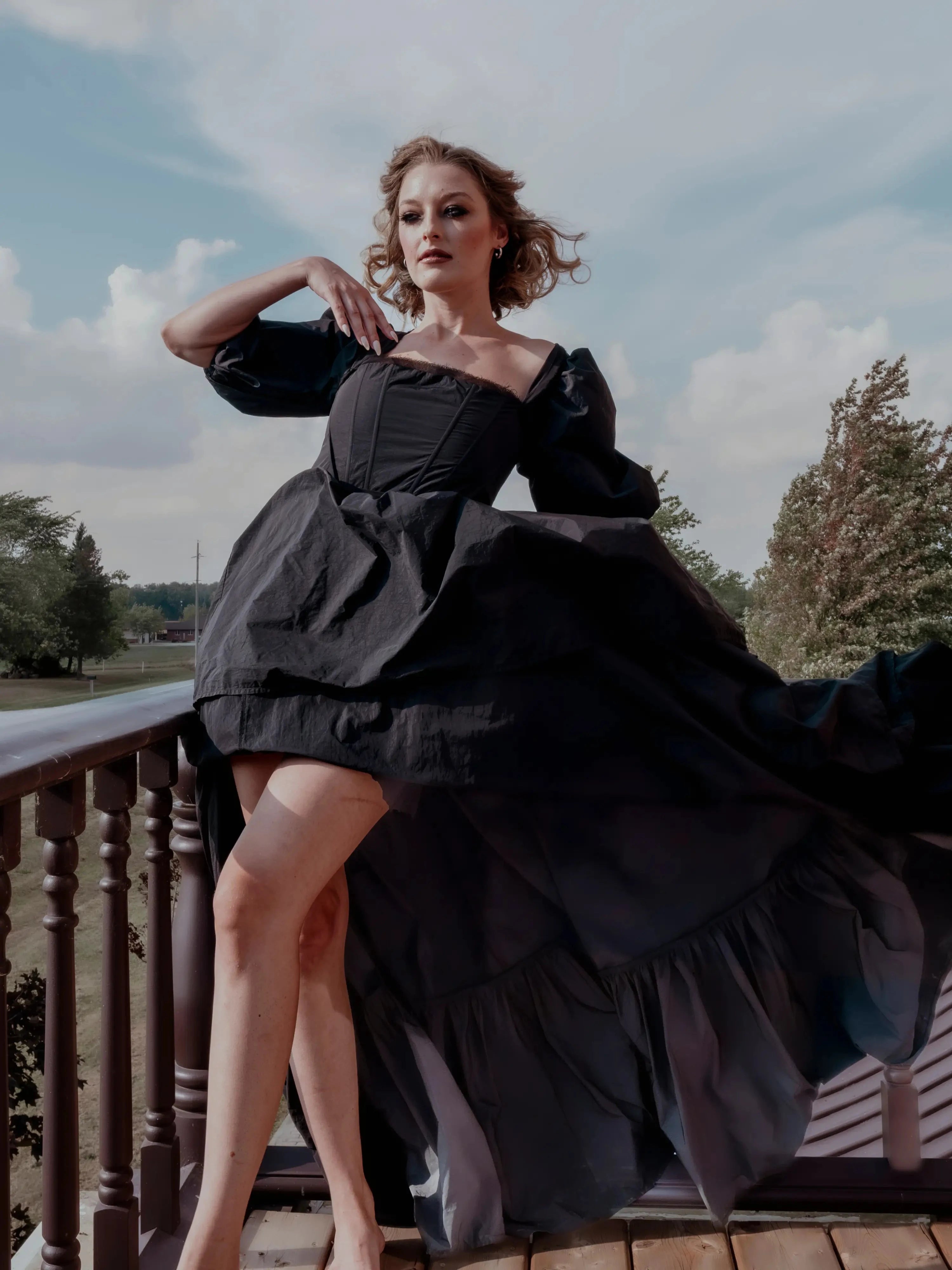 The Josephine Renaissance Gown in black with puff sleeves and corset bodice, flowing dramatically on a balcony. Gothic fairytale maxi dress style.