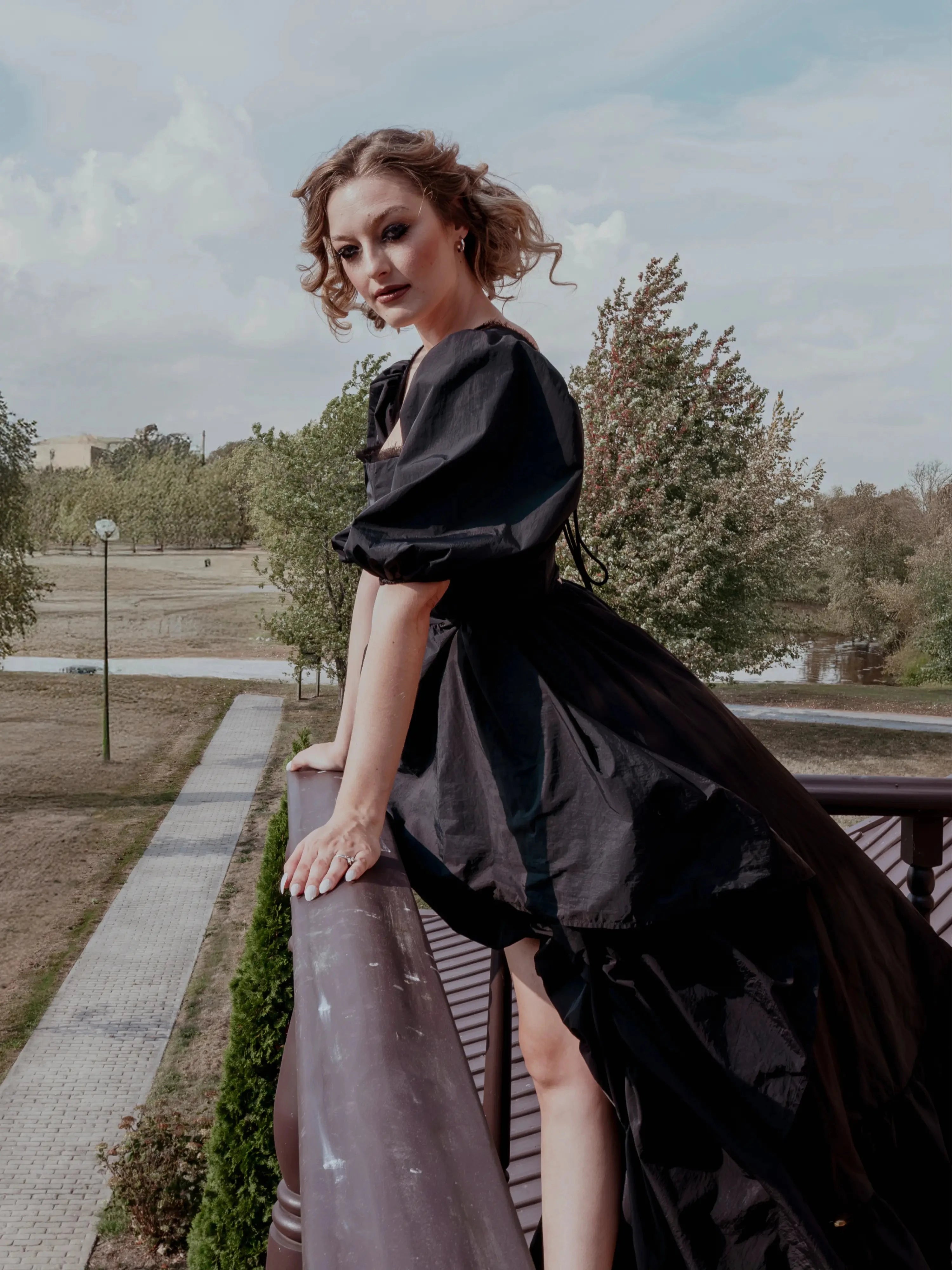 A black taffeta corset gown worn by a woman with puff sleeves and corset bodice, styled outdoors on a balcony for a gothic fairytale look.