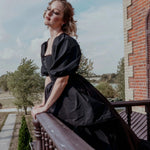 A black taffeta corset gown worn by a woman, featuring dramatic puff sleeves and a corset bodice, styled on a balcony for a gothic fairytale look.