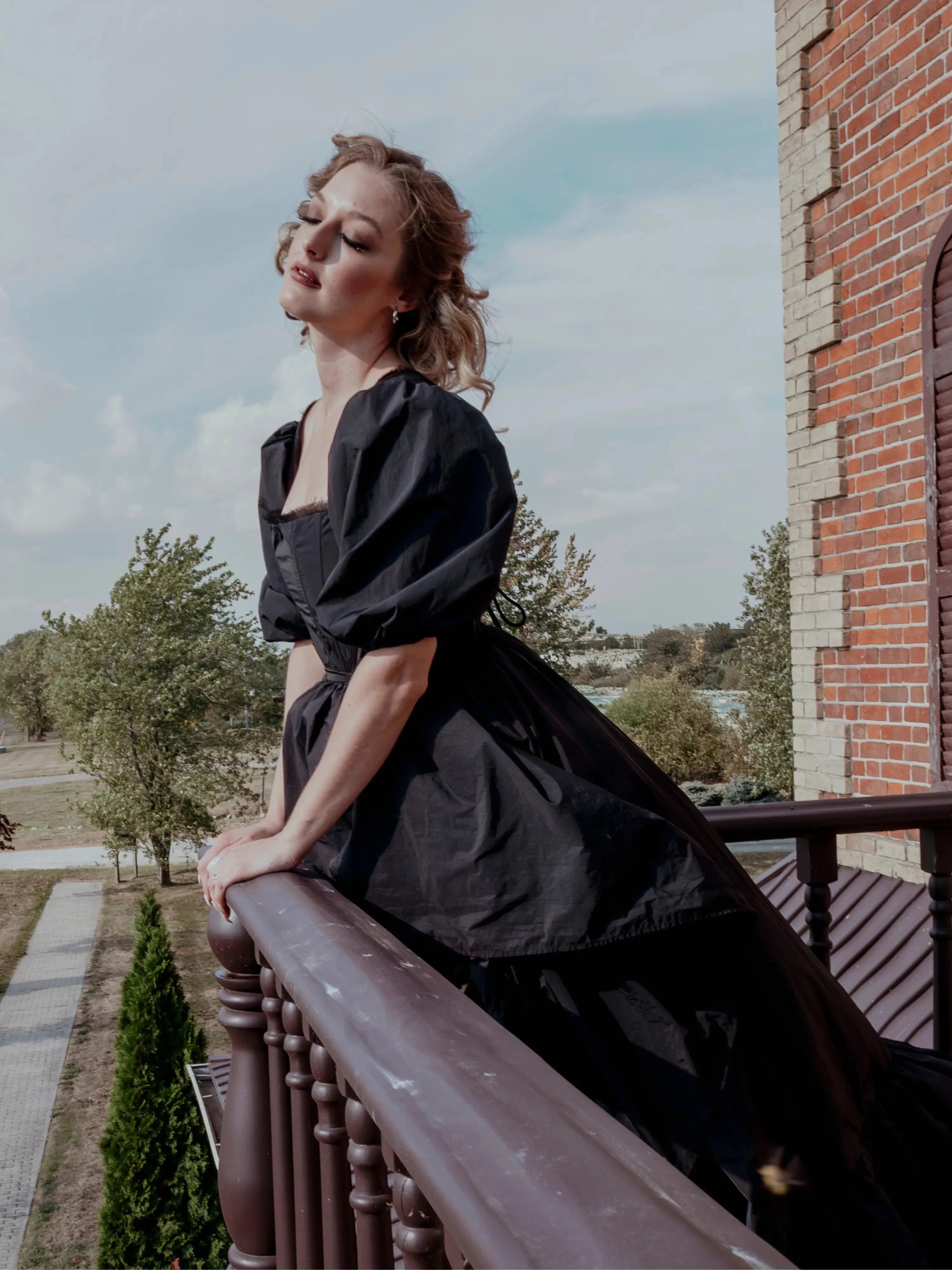 A black taffeta corset gown worn by a woman, featuring dramatic puff sleeves and a corset bodice, styled on a balcony for a gothic fairytale look.