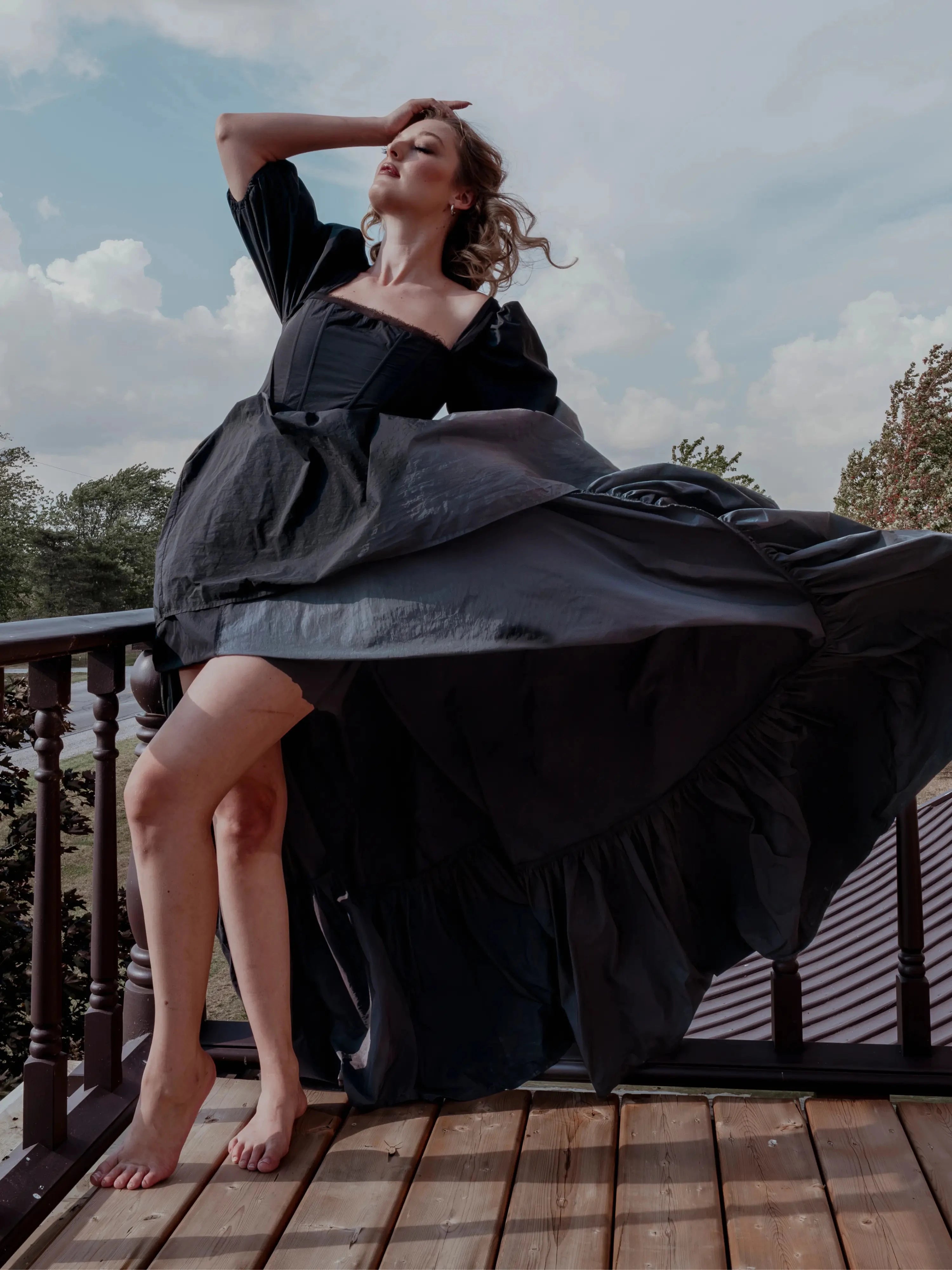 The Josephine Renaissance Gown in flowing black taffeta fabric with puff sleeves and corset bodice, captured mid-twirl on a balcony. Gothic fairytale style.