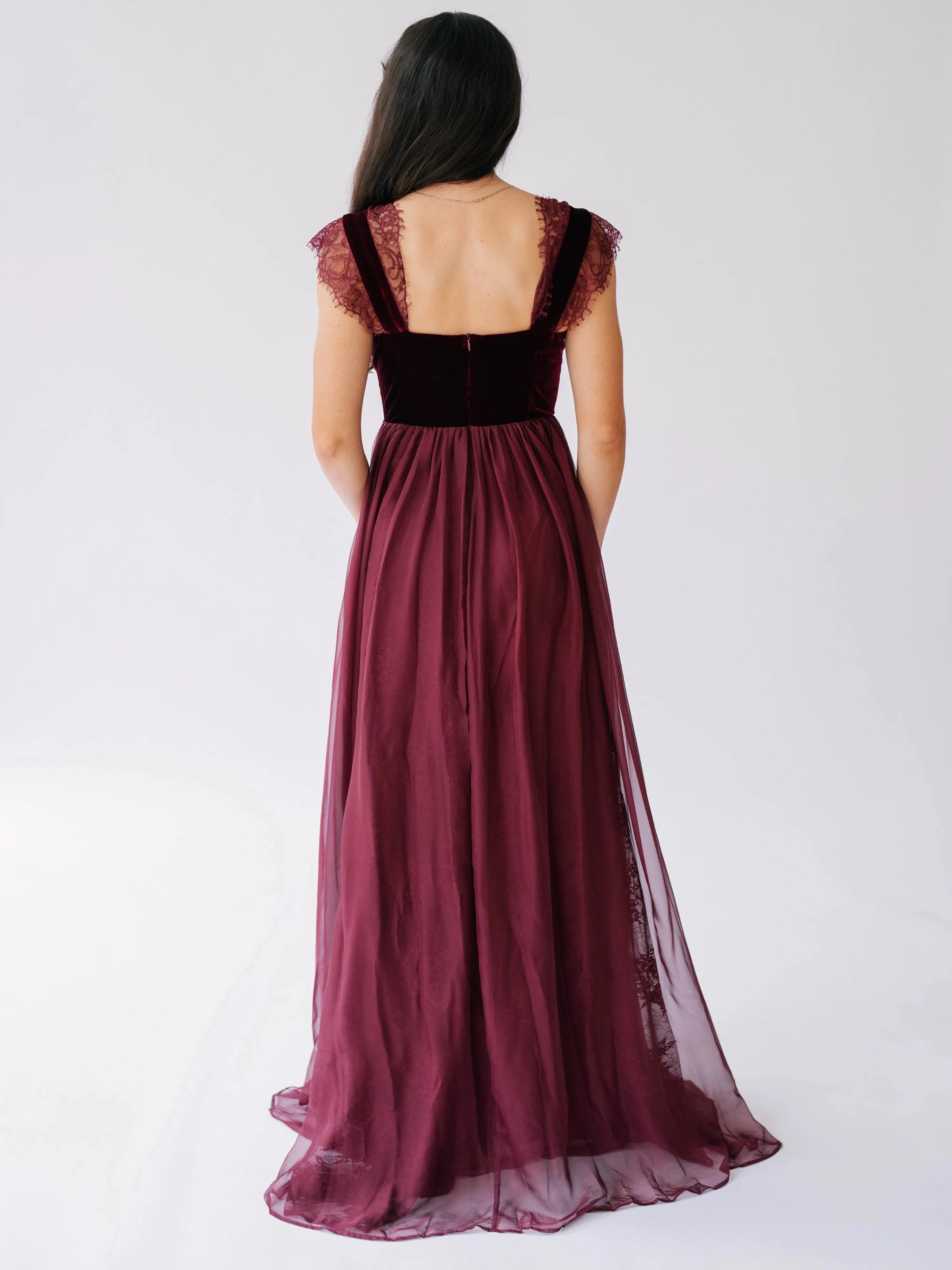 Back view of a red corset dress showing the square back and flowing chiffon skirt with a velvet bodice.