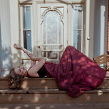The Scarlet Red Scorned Lovers Gown styled outdoors, featuring a flowing red chiffon skirt and corset bodice, evoking Victorian romance.