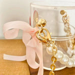 Gold-chained mini bucket bag with a pink ribbon on a wooden surface.