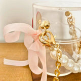 Gold-chained mini bucket bag with a pink ribbon on a wooden surface.