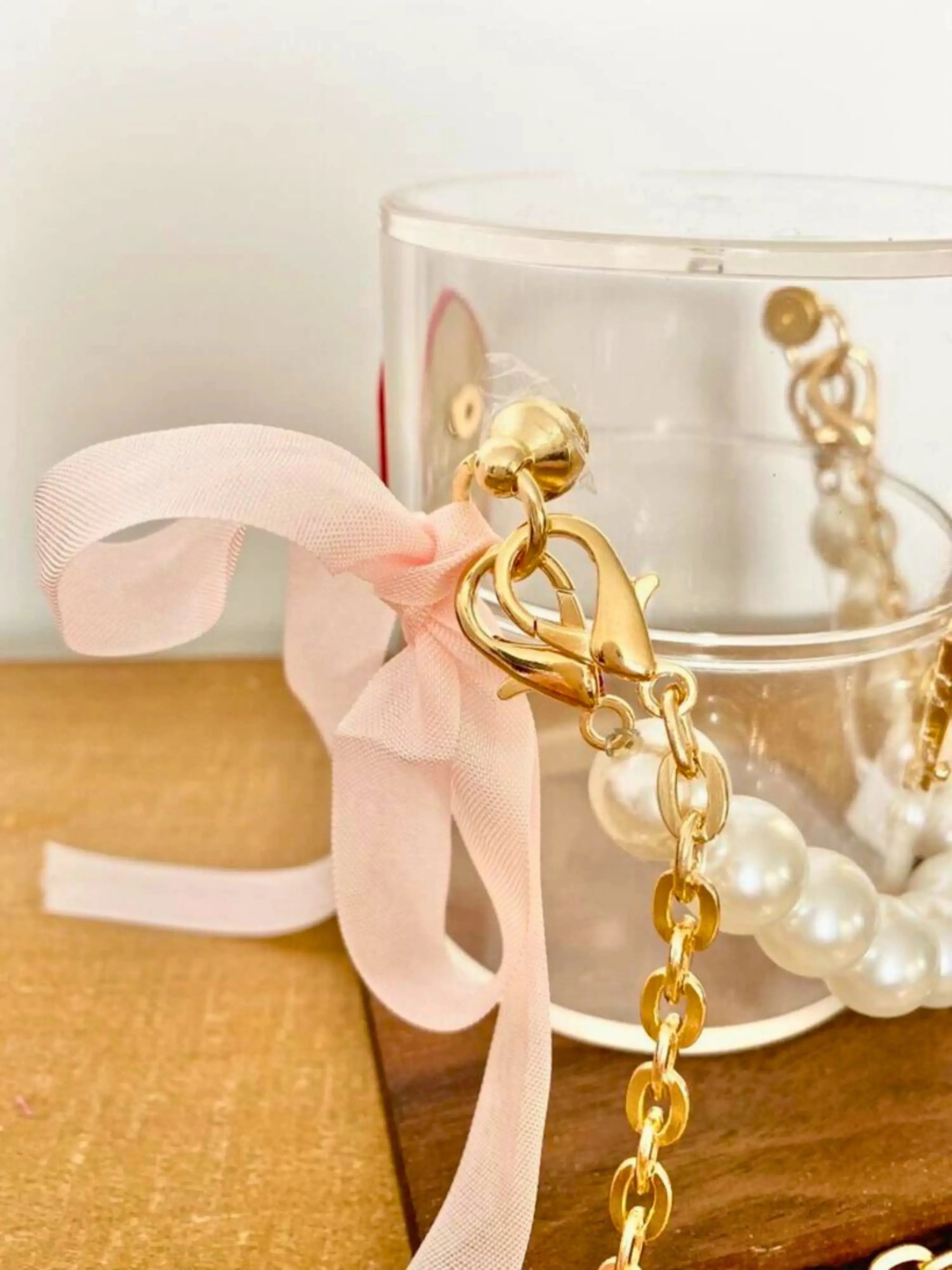 Gold-chained mini bucket bag with a pink ribbon on a wooden surface.