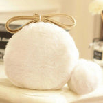 A white pom pom mini bag resting on an ivory table with books in the background.
