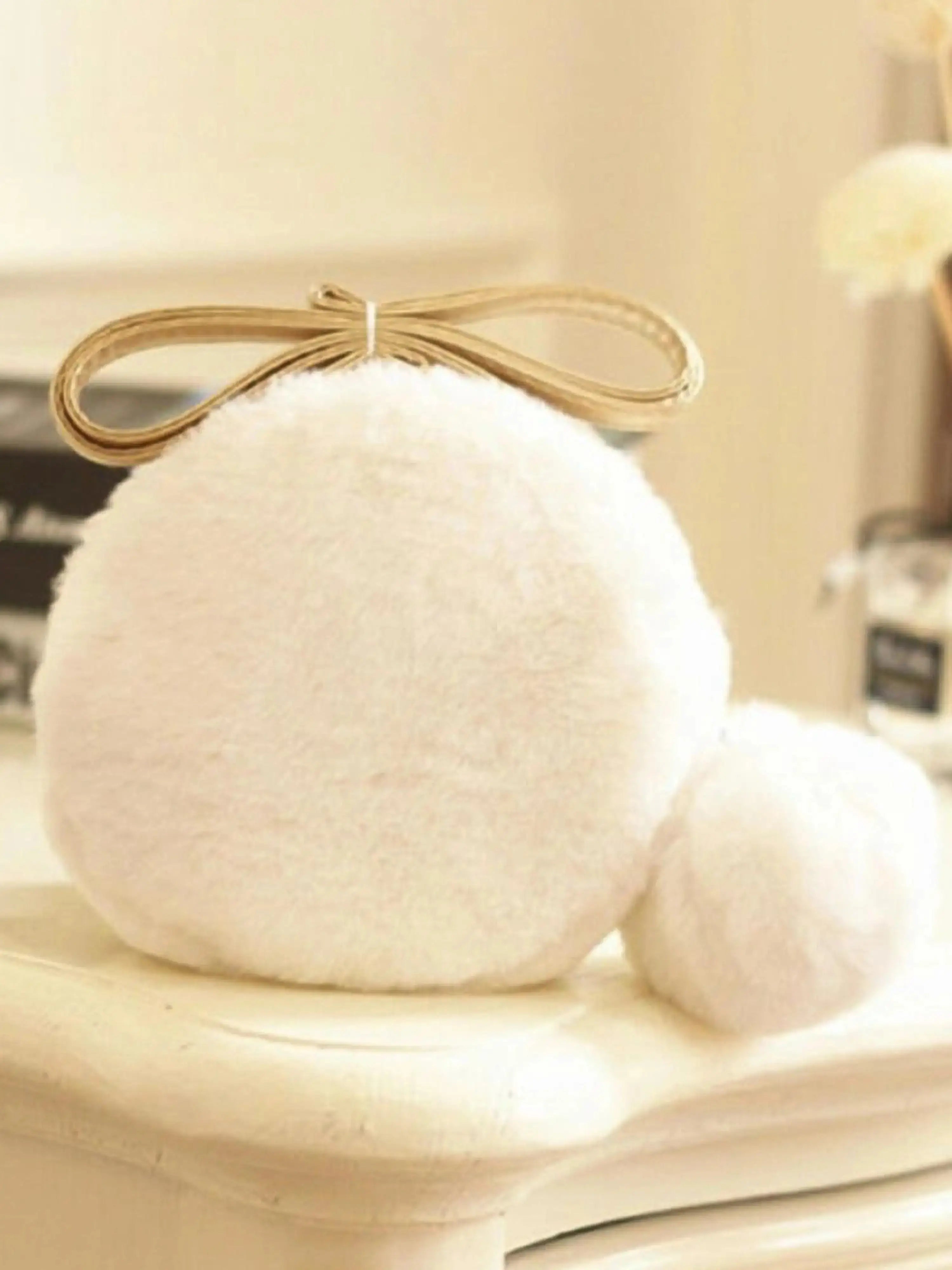 A white pom pom mini bag resting on an ivory table with books in the background.