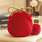 A red pom pom mini bag resting on an ivory table with books in the background.