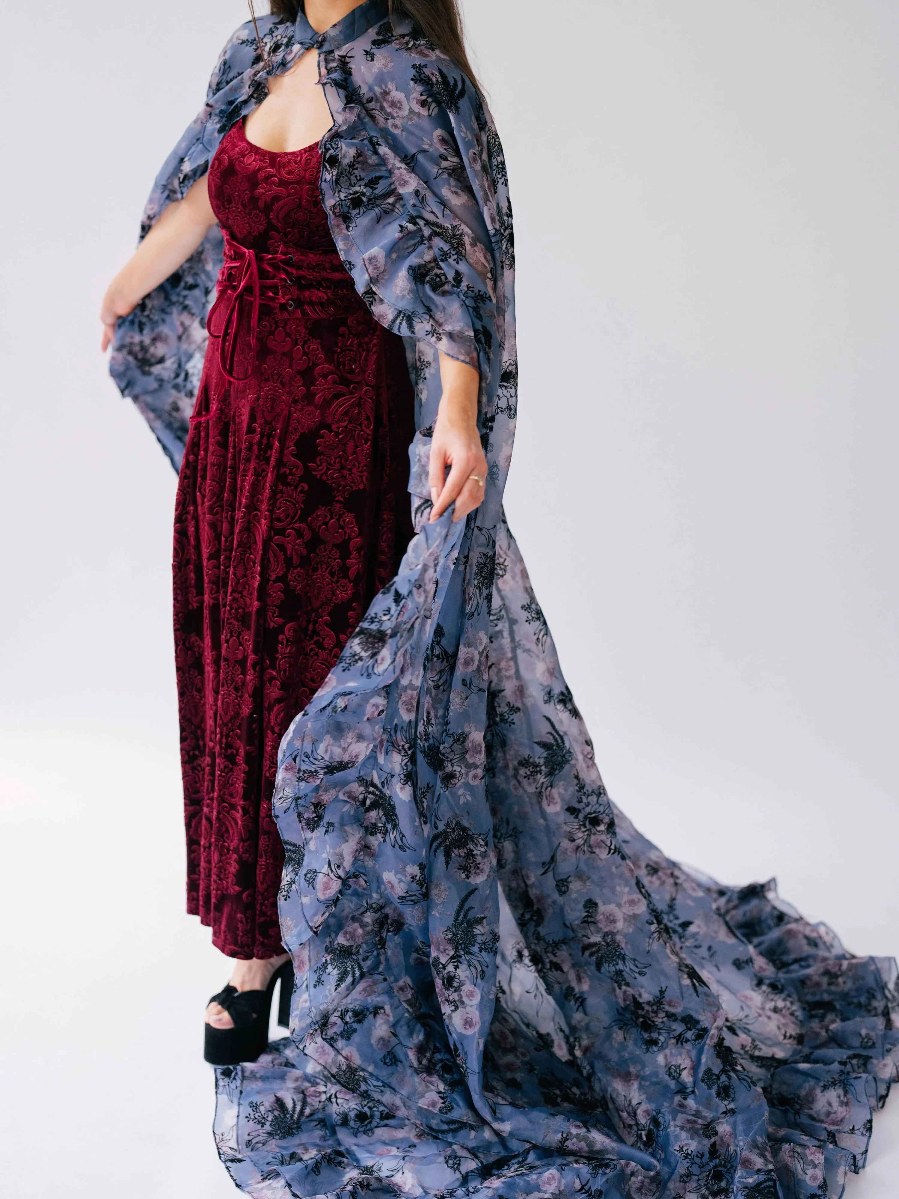 The High Priestess Victorian Cloak in sheer purple floral organza, styled over a red velvet dress with dramatic movement and volume.