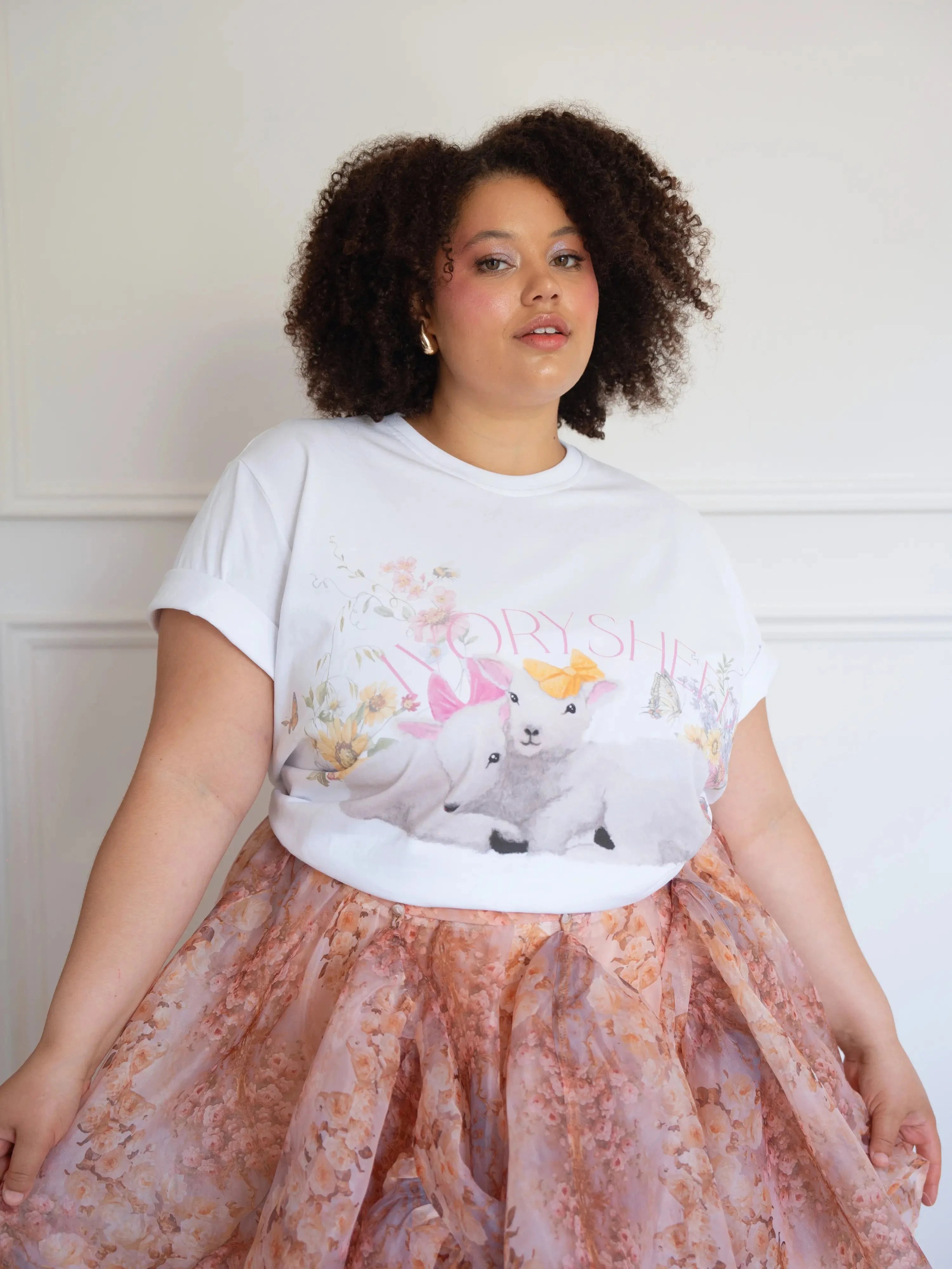The Little Lamb Tee paired with a peach floral skirt, showcasing lambs, wildflowers, and butterflies in a soft cottagecore aesthetic.