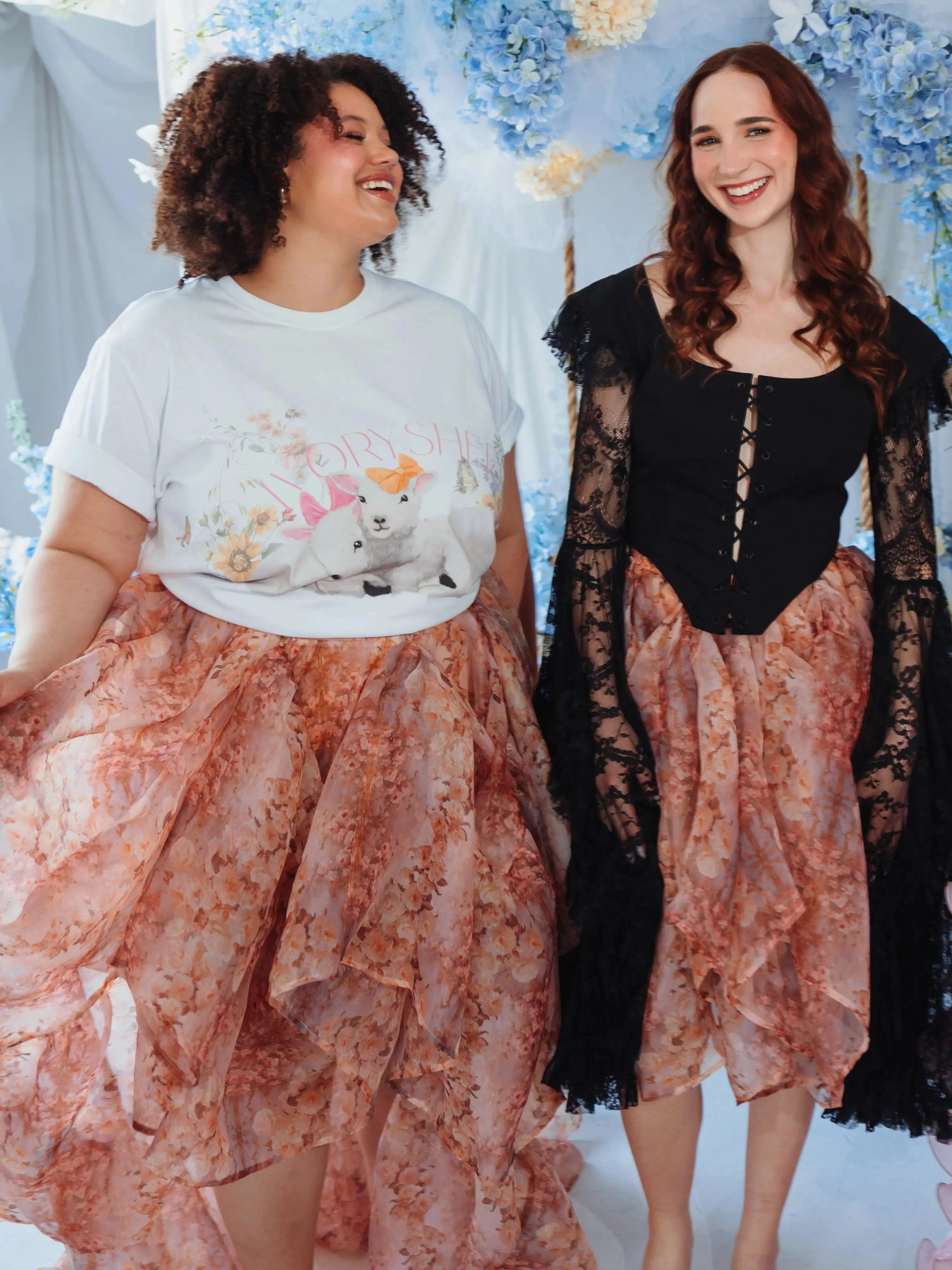 Two women wearing The Twilight Bloom Bustle Skirt in a floral organza fabric, styled with a graphic tee and a black lace corset top.