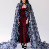 A red velvet dress worn by a woman with a sheer floral cape. A dramatic gothic look for formal or costume occasions.