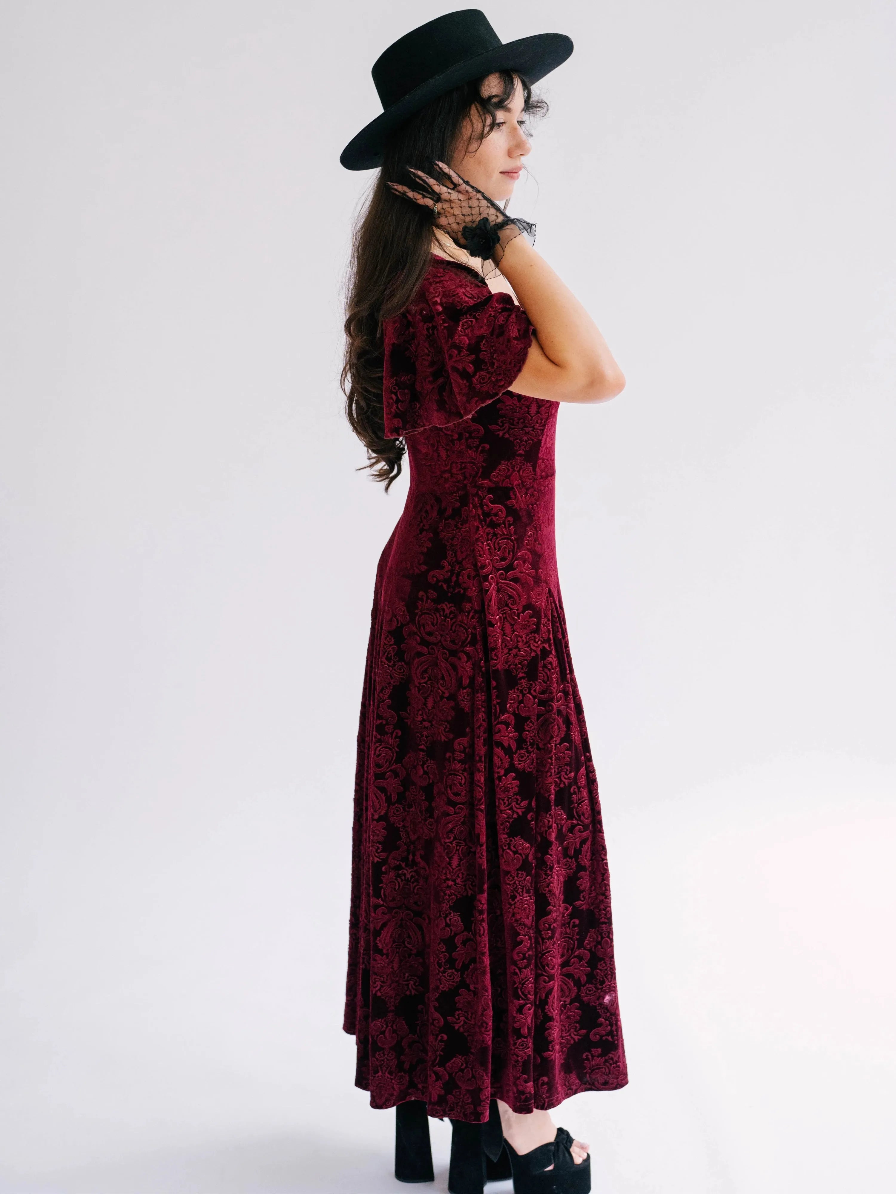 Side view of a woman wearing The Scarlet Red Velvet Viola Dress highlighting its flowing midi length and butterfly sleeves.
