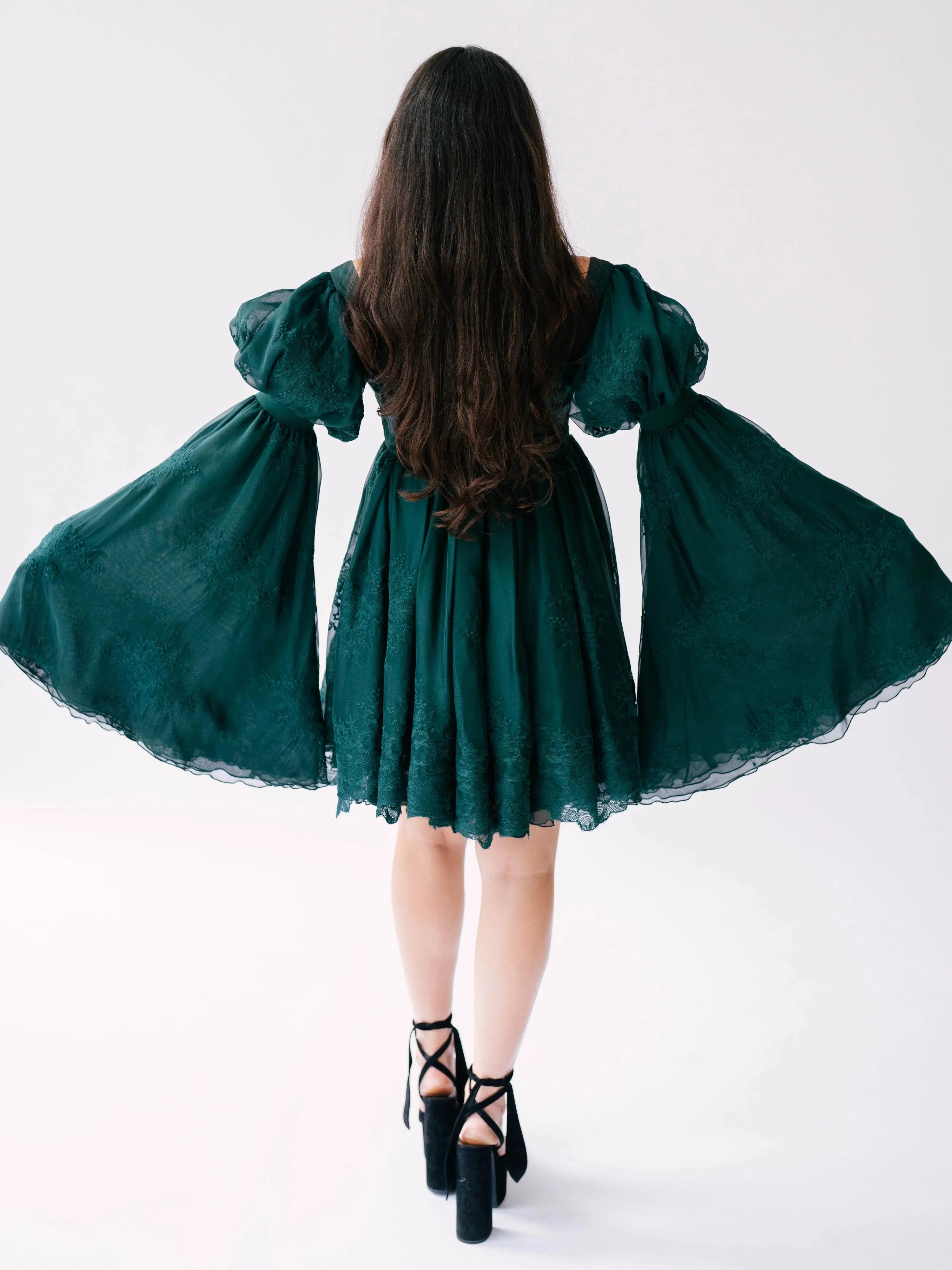 Back view of a woman wearing a green bell sleeve dress on a white background.