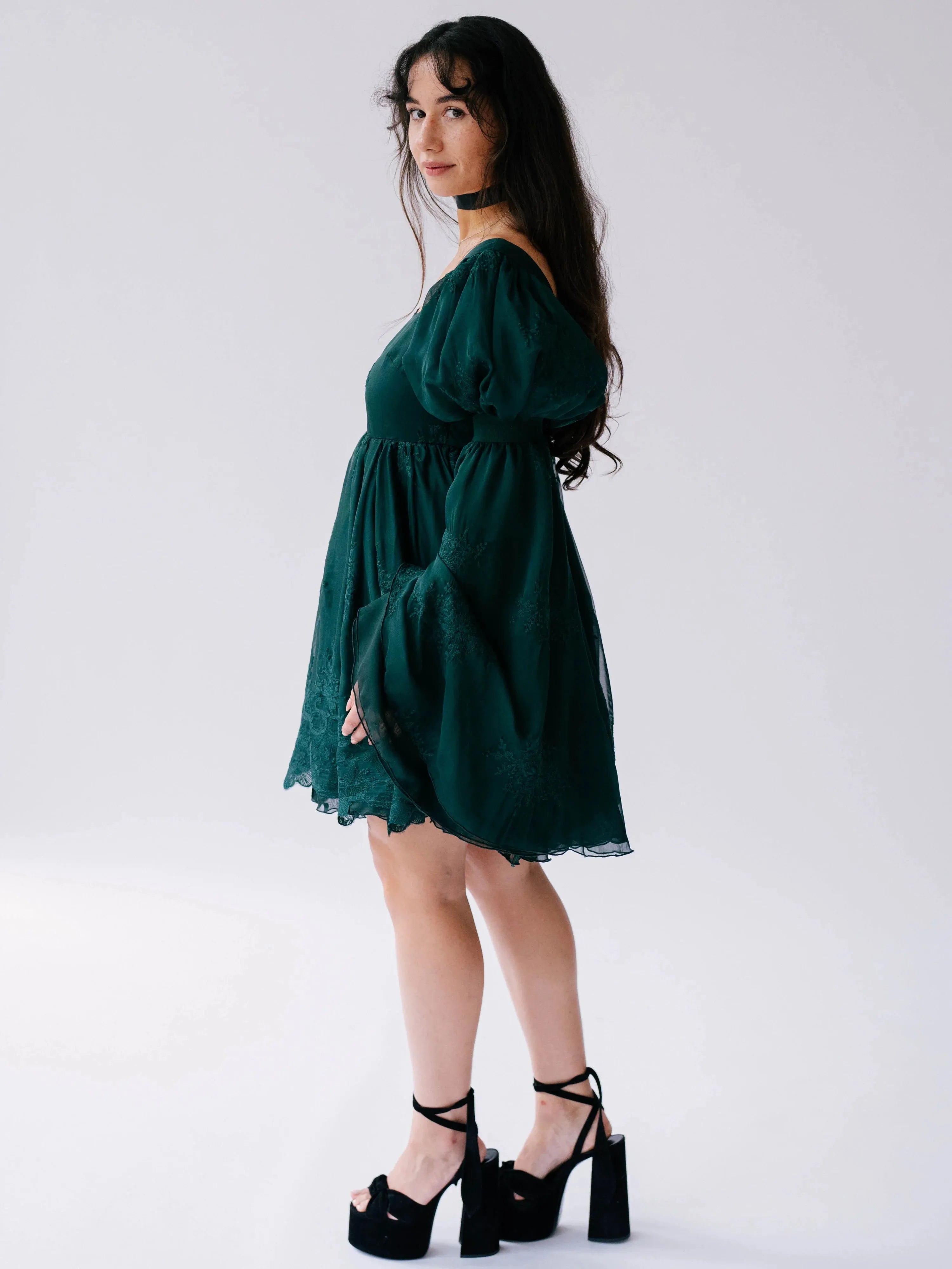 A woman wearing a green bell sleeve mini dress on a white background.