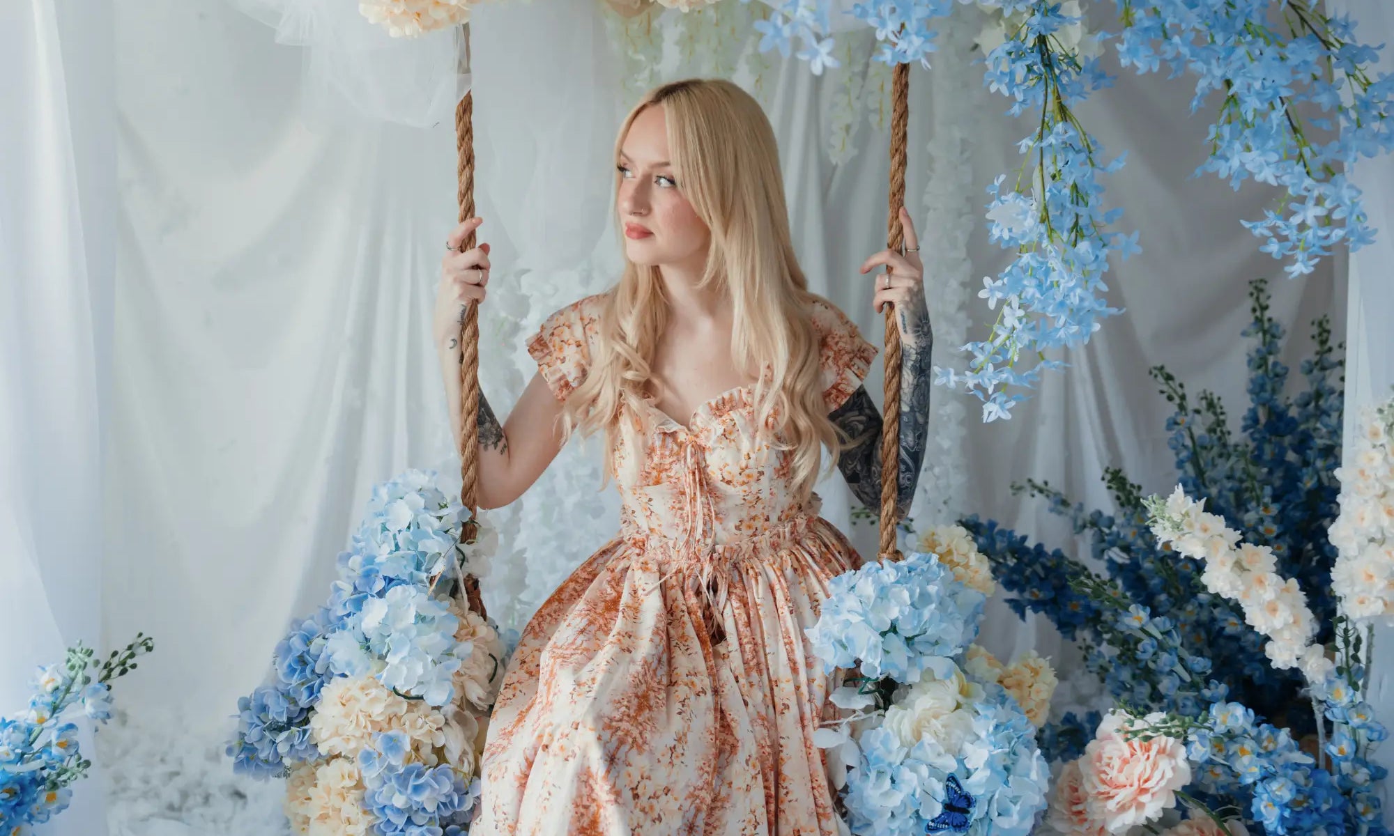 A woman sitting on a swing surrounded by florals in a cotton maxi dress.