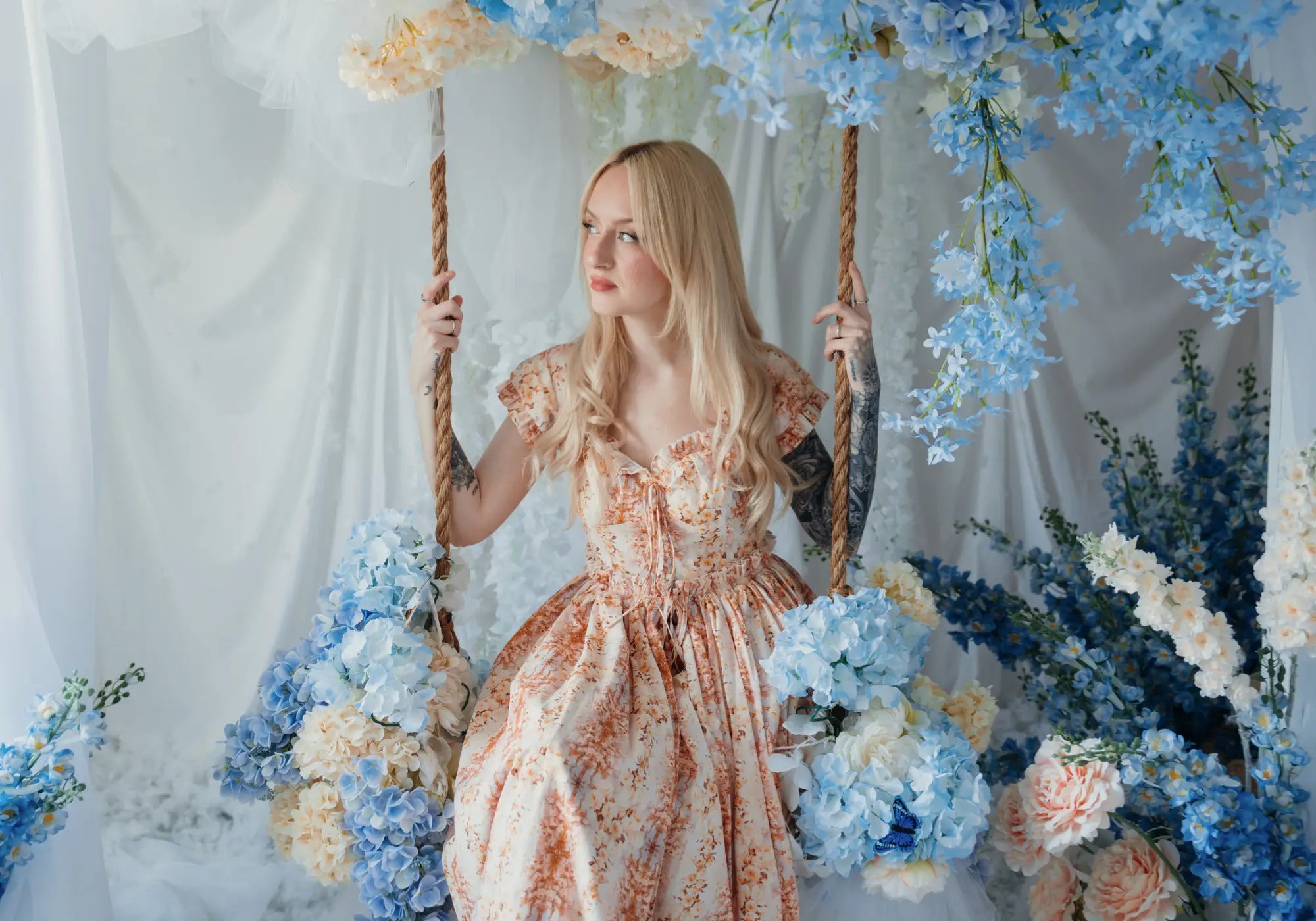 A woman sitting on a swing surrounded by florals in a cotton maxi dress.